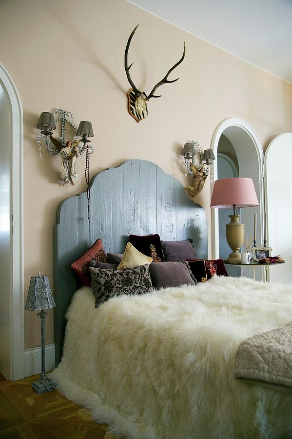 White Fur Blanket On French Bed With Rustic Wooden Headboard Against Wall With Two Sconce Lamps And Antlers Photograph by Winfried Heinze