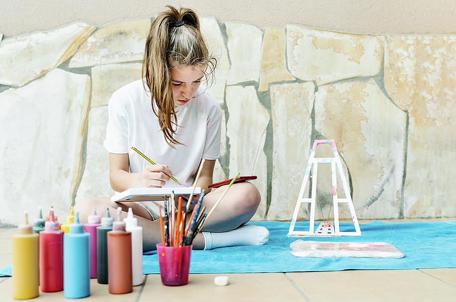 Abstract Photograph - White Girl Painting A Picture Sitting On A Terrace With All Painting Elements Around As Brushes, Paintings, Water, Easel.. by Cavan Images