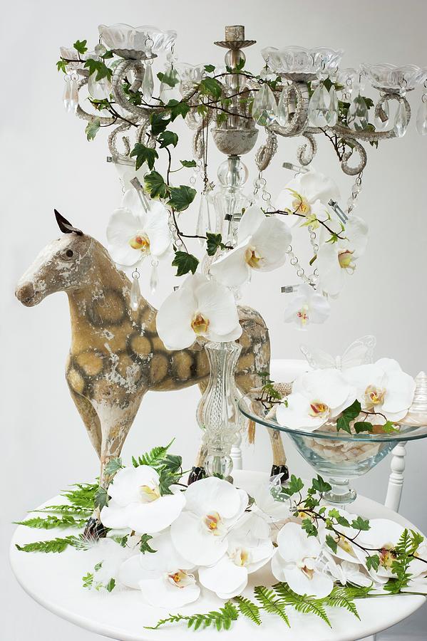 White Orchids In A Bowl And On A Candle Holder With Glass Decorations And An Antique Miniature Horse Behind It On A White Table Photograph by Linda Burgess