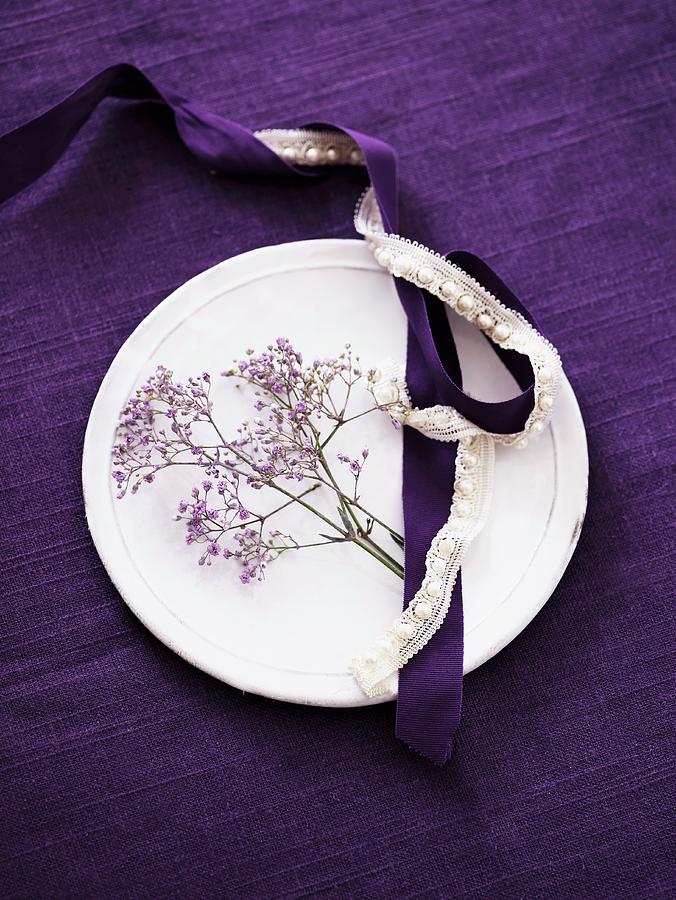 White Plate On Purple Tablecloth Decorated With Purple Flowers And Satin And Lace Ribbons Photograph by Mikkel Adsbl