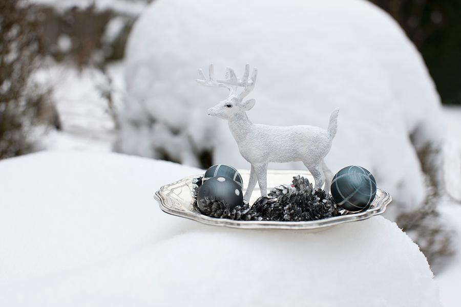 White Stag Ornament, Metal Fir Cones And Christmas Tree Baubles On Plate Surrounded By Snow Photograph by Sabine Lscher