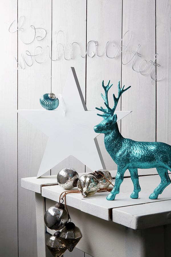 White Wooden Table With White Wooden Star, Turquoise Glittery Reindeer, Silver Baubles And Christmas Motto Formed From Wire In Background Photograph by Mona Binner Photographie