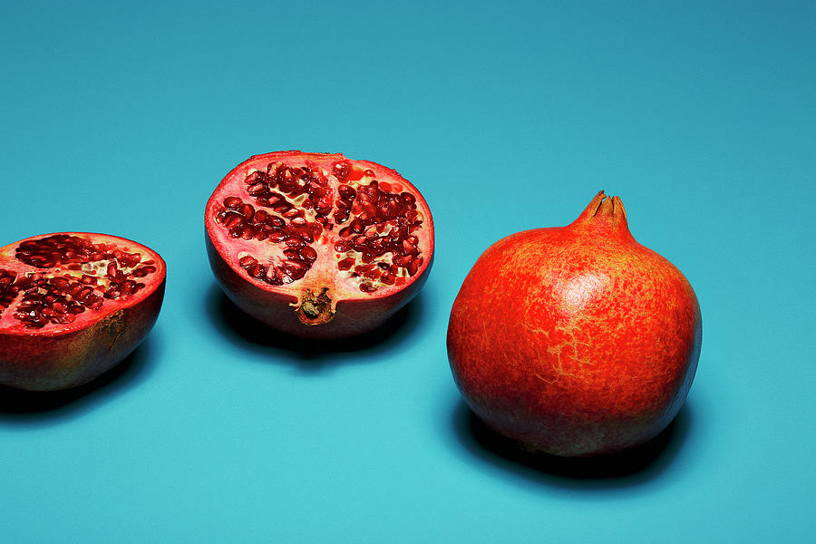 Whole And Halved Pomegranates In Front Of A Blue Background Photograph by Roberto Rabe