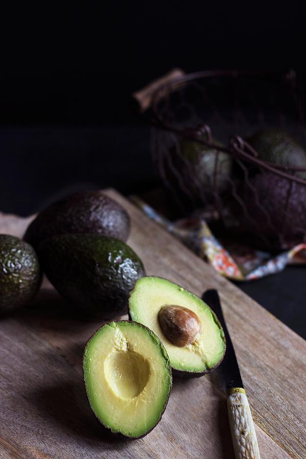 Whole Avocados And A Halved Avocado On A Wooden Board Photograph by Vernica Orti