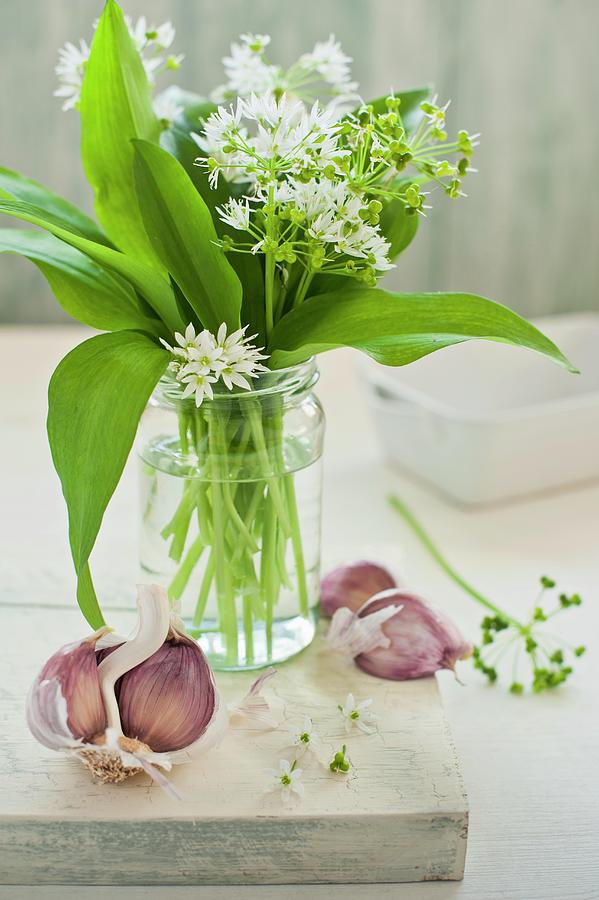 Wild Garlic With Flowers In A Glass Of Water With Garlic Cloves On A Chopping Board Photograph by Magdalena Hendey