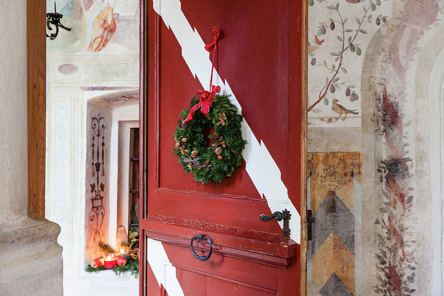 Wintry Decorations In Entrance Area: Arrangement In Window Niche And Wreath On Red Wooden Door Photograph by Anneliese Kompatscher