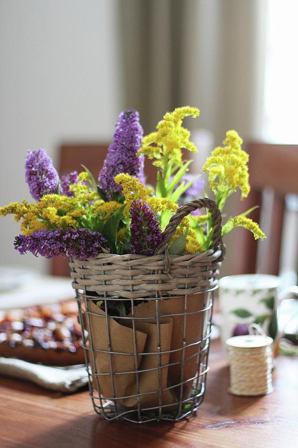 Wire Basket Of Yellow And Purple Flowers Decorating Table Photograph by Sylvia E.k Photography