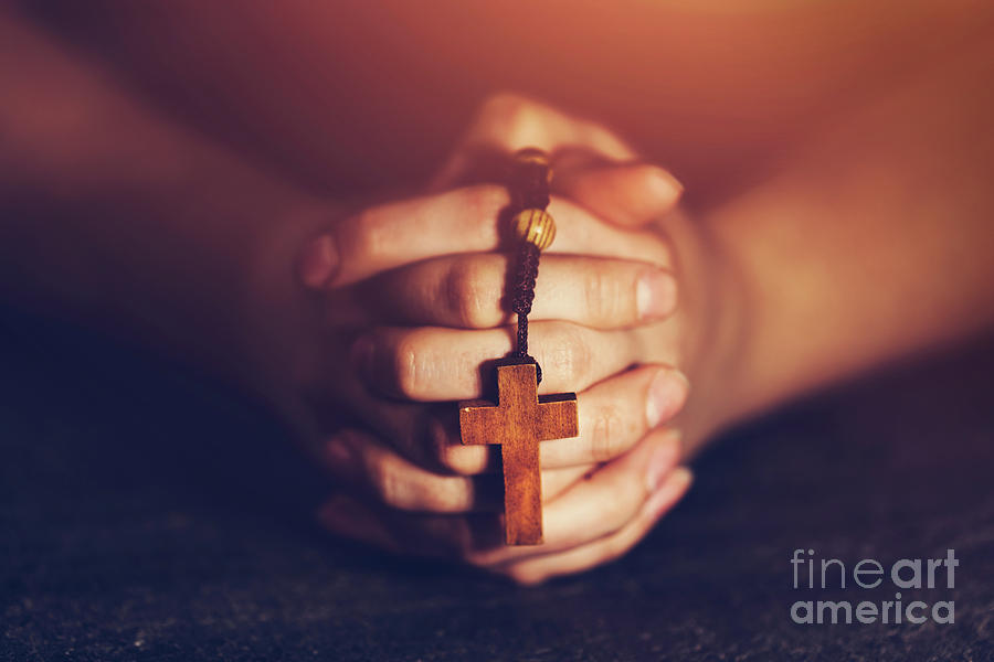 Woman holding a rosary and praying. Photograph by Michal Bednarek
