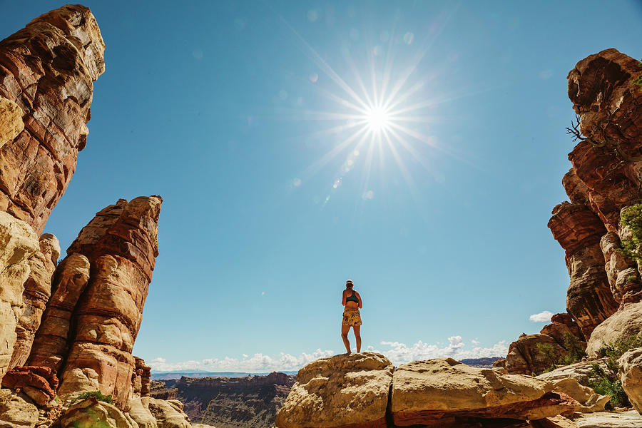 Woman In Sports Bra And Shorts Stands On Rocks In Desert Under Sun