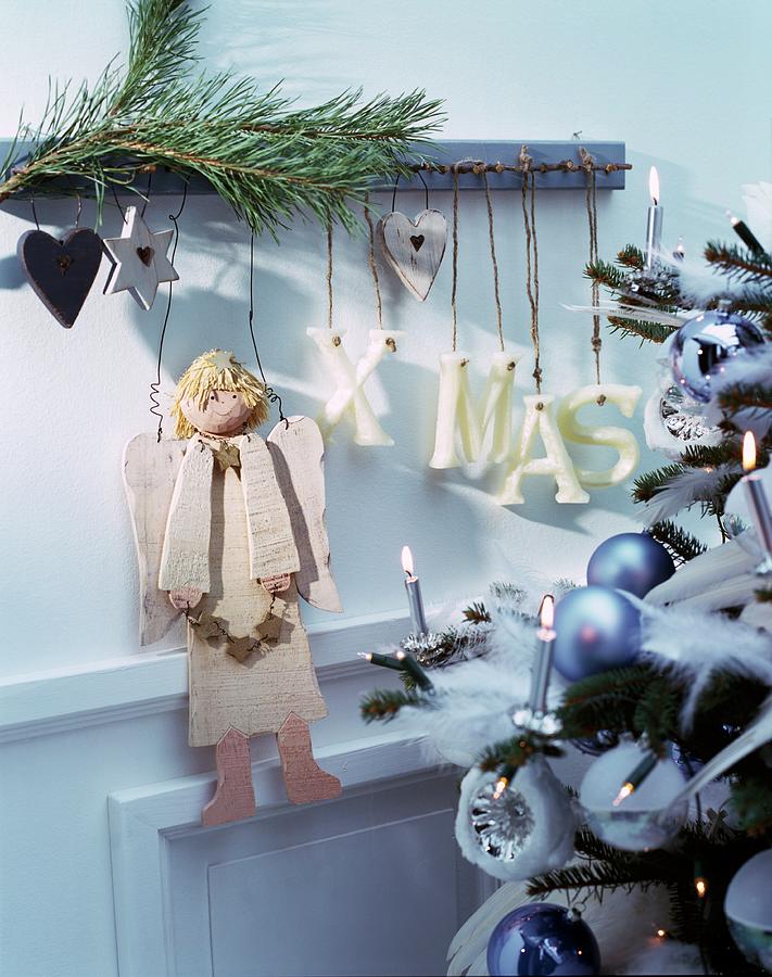 Wooden Christmas Angel And Letters Spelling Xmas Hung From Rustic Coat Rack Next To Christmas Tree Decorated In Pastel Blue Photograph by Matteo Manduzio