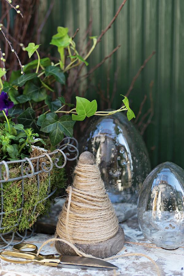 Wooden Cone Of Twine, Scissors And Glass Eggs Next To Easter Arrangement In Wire Basket Photograph by Cecilia Mller