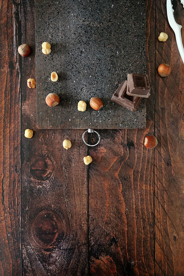 Wooden Cutting Board On Table With Hazelnuts And Chocolate Photograph by Claudia Gargioni