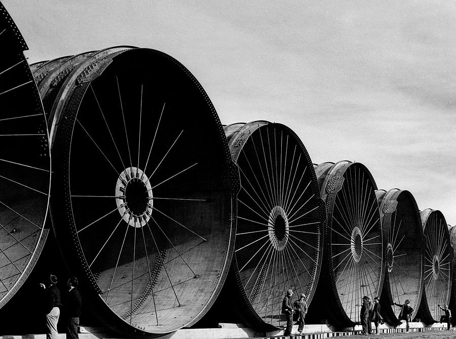 Workmen looking over gigantic pipe segments awaiting installation for purposes of diverting a section of the Missouri River during construction of the Fort Peck dam. Photograph by Margaret Bourke-White