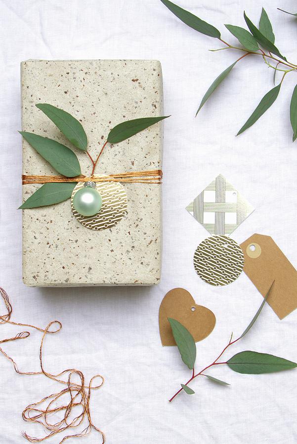 Wrapped Gift Decorated With Christmas Bauble And Sprig Of Leaves Photograph by Marij Hessel