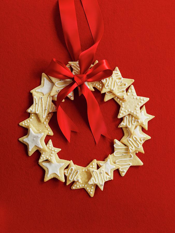 Wreath Made Of Star Cookies With A Red Ribbon In Front Of A Red Background Photograph by Gareth Morgans