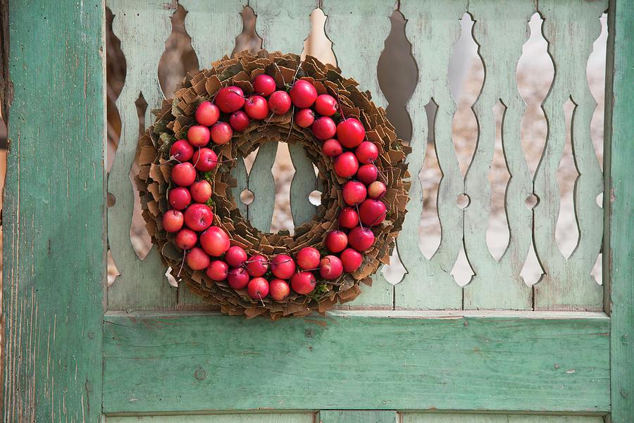 Wreath Of Bark And Small Red Apples Hung On Weathered Wooden Door Photograph by Inge Ofenstein