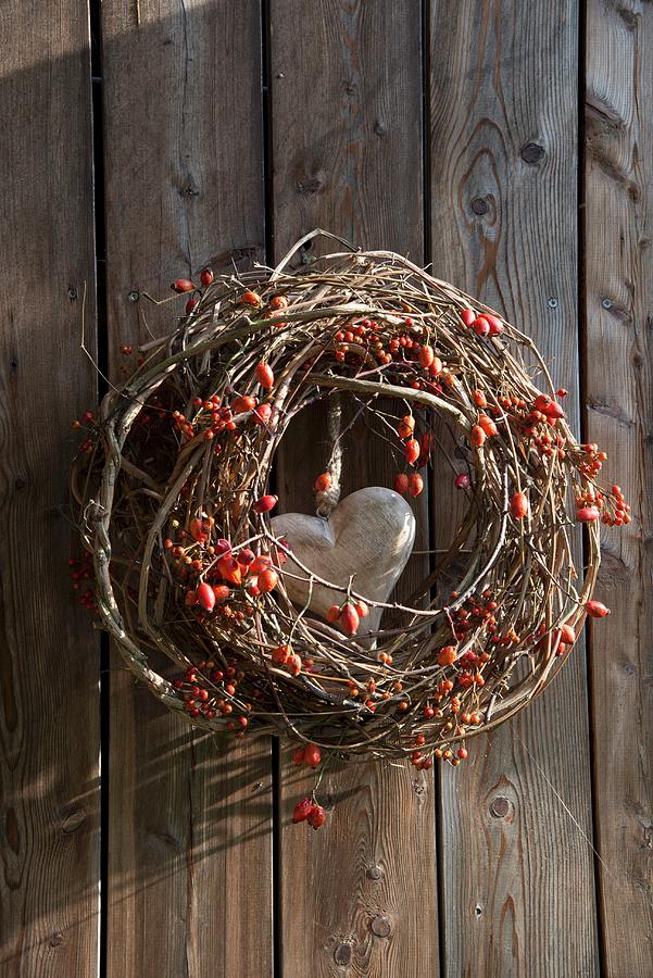 Wreath Of Berries, Branches And Rose Hips With Wooden Love-heart In Centre Hung On Wooden Wall Photograph by Inge Ofenstein