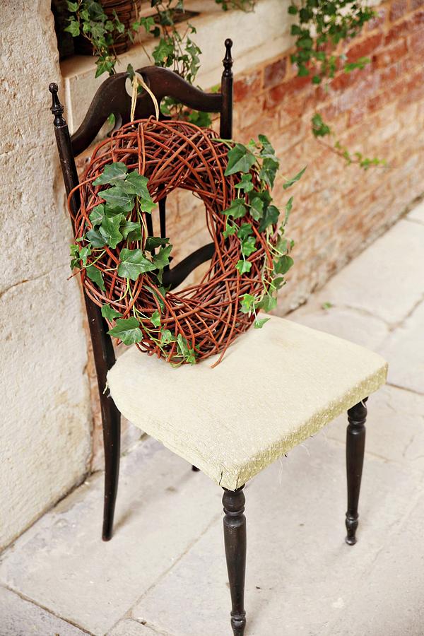 Wreath Of Wicker And Ivy On Chair Against Brick Wall Photograph by Alexandra Panella