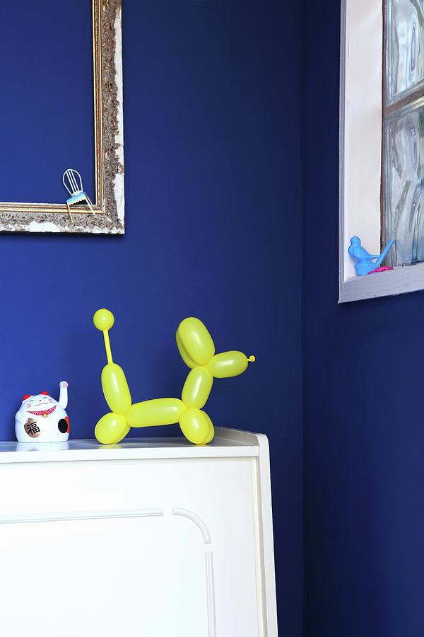 Yellow Balloon-dog Ornament In Front Of Royal Blue Wall Photograph by Thordis Rggeberg