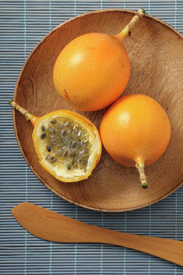 Yellow Passion Fruits, Whole And Halved, On A Wooden Plate Photograph by Jean-christophe Riou