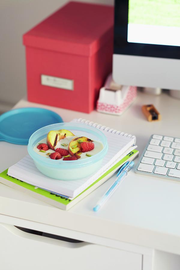 Yoghurt With Raspberries, Grilled Apples And Pistachios In A Tupperware Bowl On A Desk Photograph by Charlotte Tolhurst