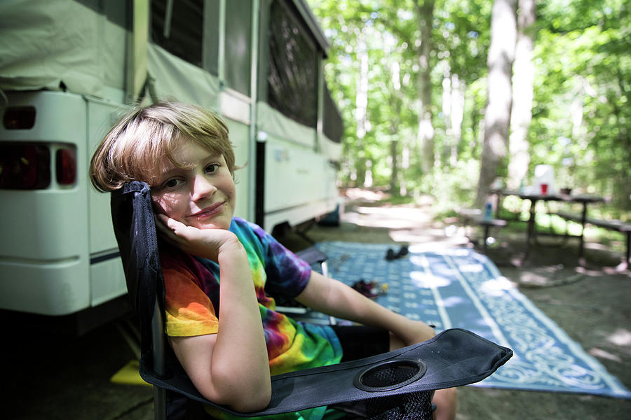 Nature Photograph - Young Boy In Tie Dye Shirt Sits In Camping Chair In Front Of Pop Up by Cavan Images