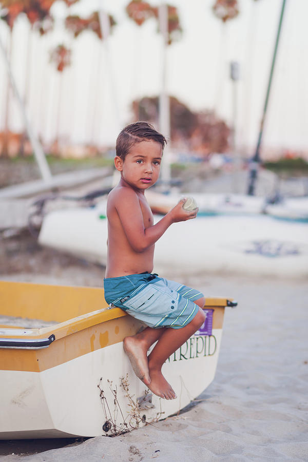 Young Boy Sitting On A Docked Boat At The Beach And Holding A Ball ...