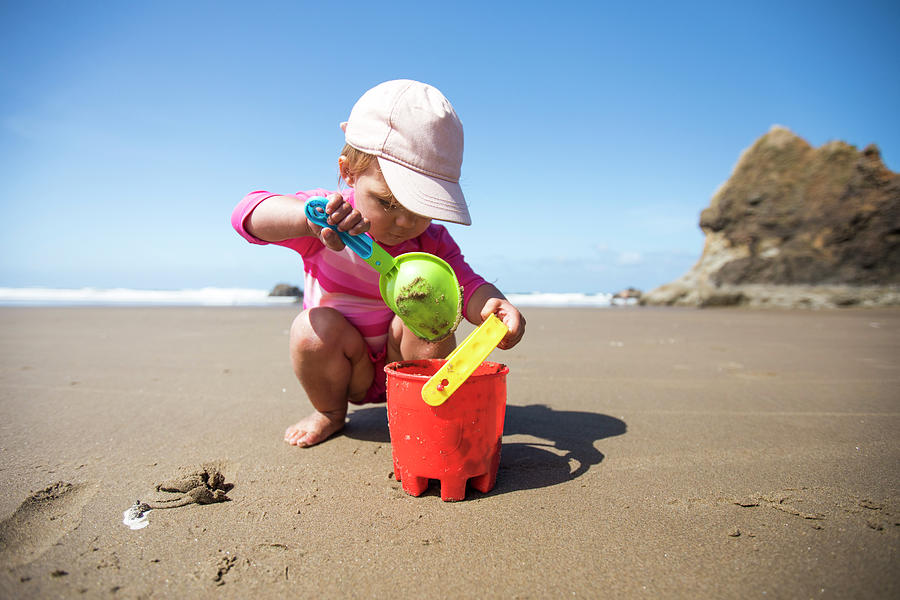 Young Girl Shovelling Sand Into Bucket At The Beach. Photograph by ...