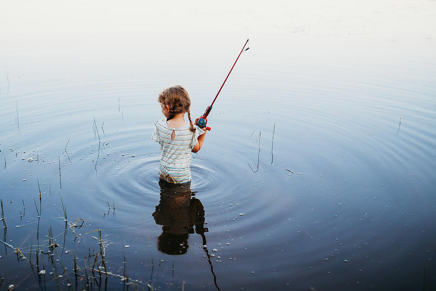 Young Girl Standing In Water At Lake Holding Fishing Pole
