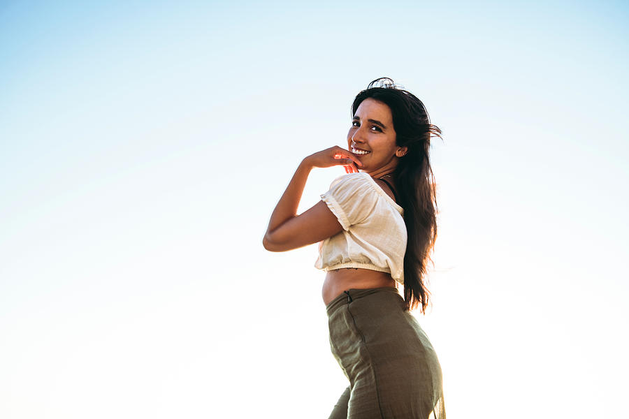 Young Latina Woman Smiling By The Ocean At Golden Hour In Summertime