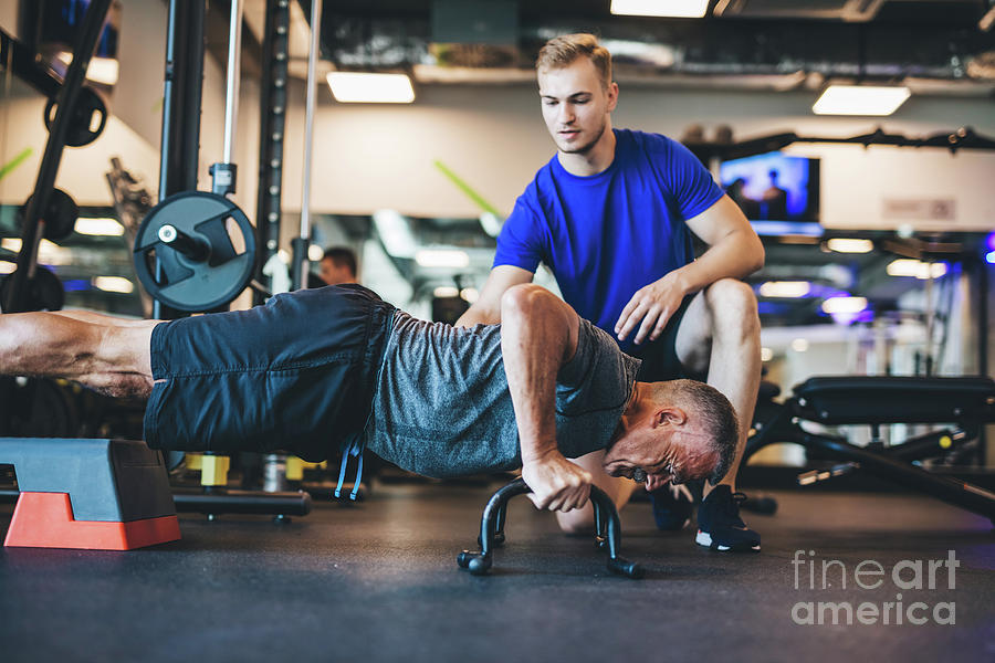 Young man helping senior man in a workout. Photograph by Michal Bednarek