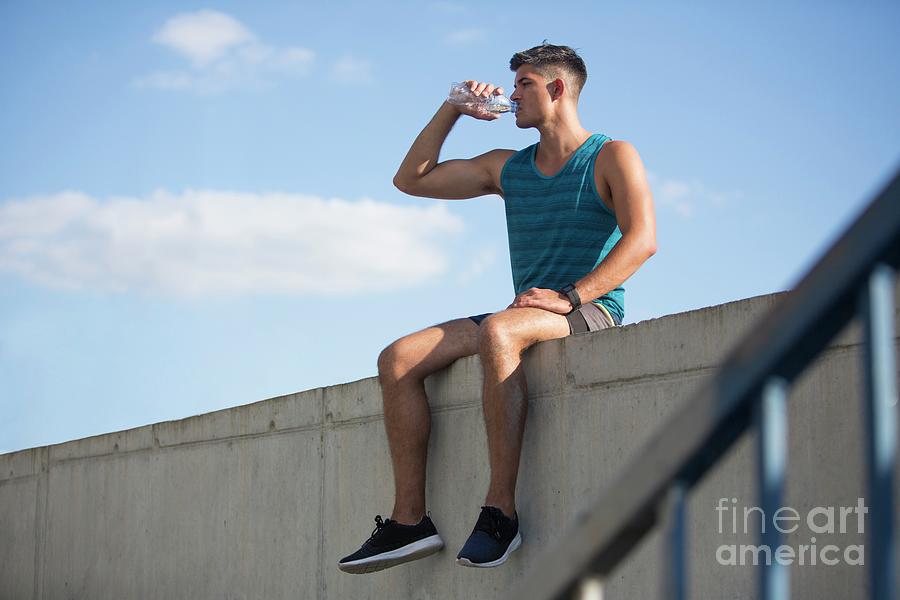 Young Man Sitting On Wall Drinking Bottle Of Water Photograph by Science Photo Library