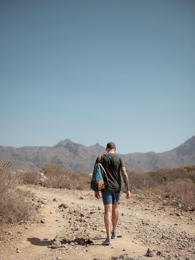 Young Man With Backpack Walking Through Desert Landscape To Mouuntains ...