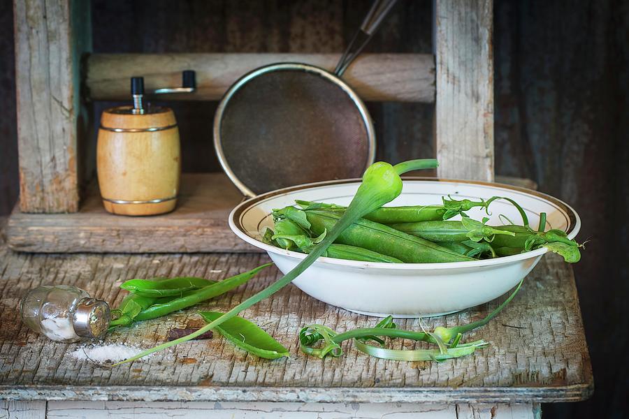 Young Pea Pods In A Bowl On An Old Wooden Table With A Spilt Salt Shaker Photograph by Natasha Breen