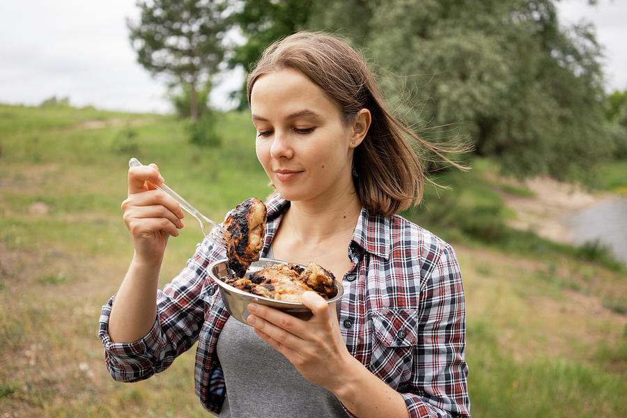 Young Woman Eating Hot Grilled Chicken Against Trees In Forest ...