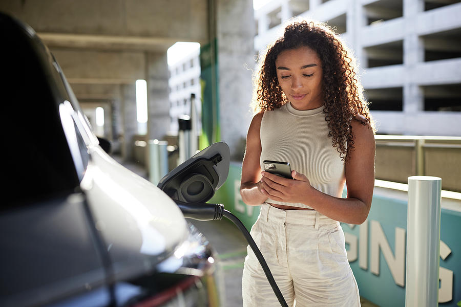 Young Woman Using Phone By Car Getting Charged At Parking Garage ...