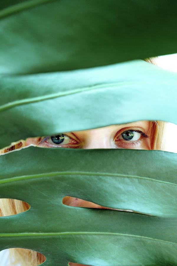 Nature Photograph - Young Woman With Blue Eyes Looking Through Green Palm Leaf by Cavan Images