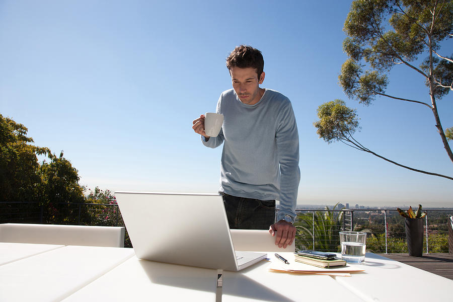  Man drinking coffee with working from home on balcony  Photograph by Tom Merton
