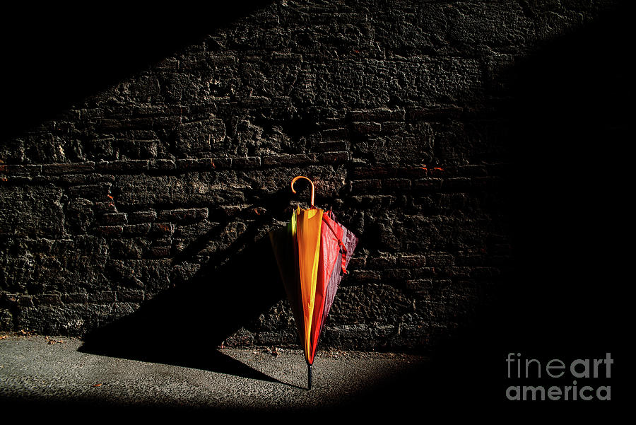 A beautiful colored umbrella rests folded against a brick wall i #1 Photograph by Joaquin Corbalan