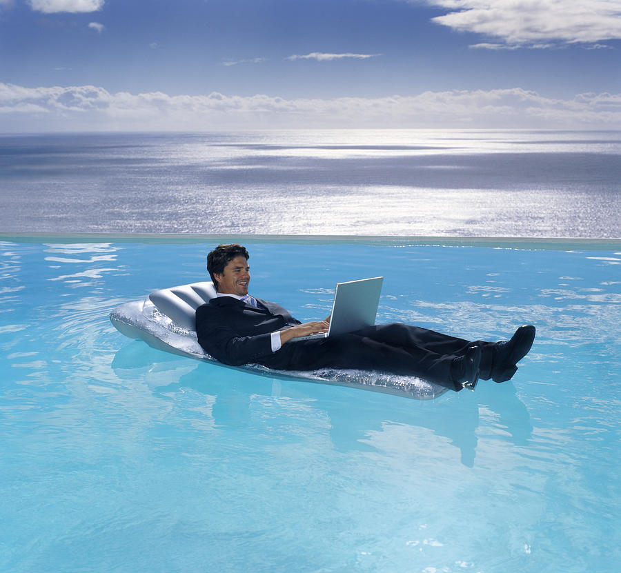A man in a suit on a lilo in a swimming pool, a laptop on his lap. #1 Photograph by Mint Images