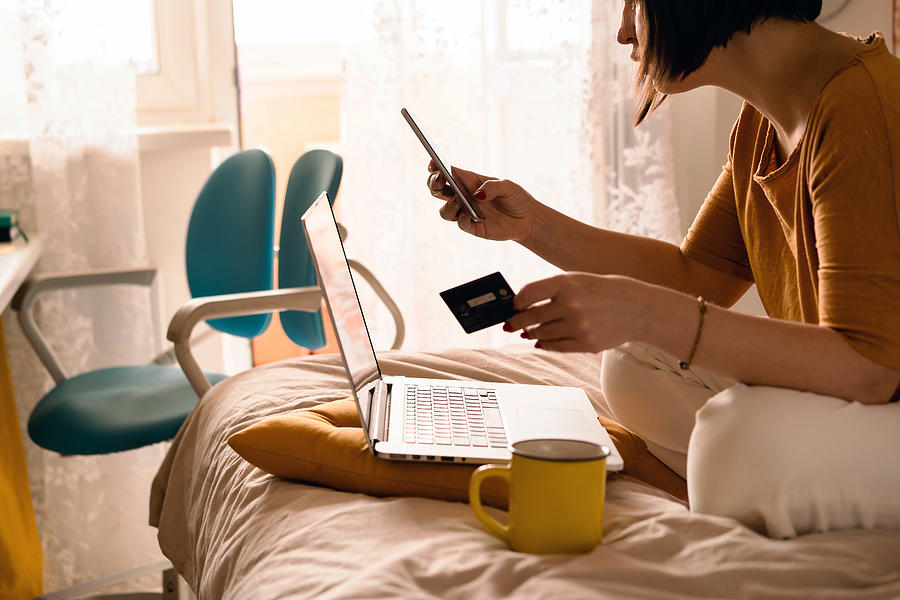 A middle-aged woman in white jeans and a yellow sweater sitting on the bed in a yoga pose in front of a laptop and a cup of coffee #1 Photograph by Fiordaliso