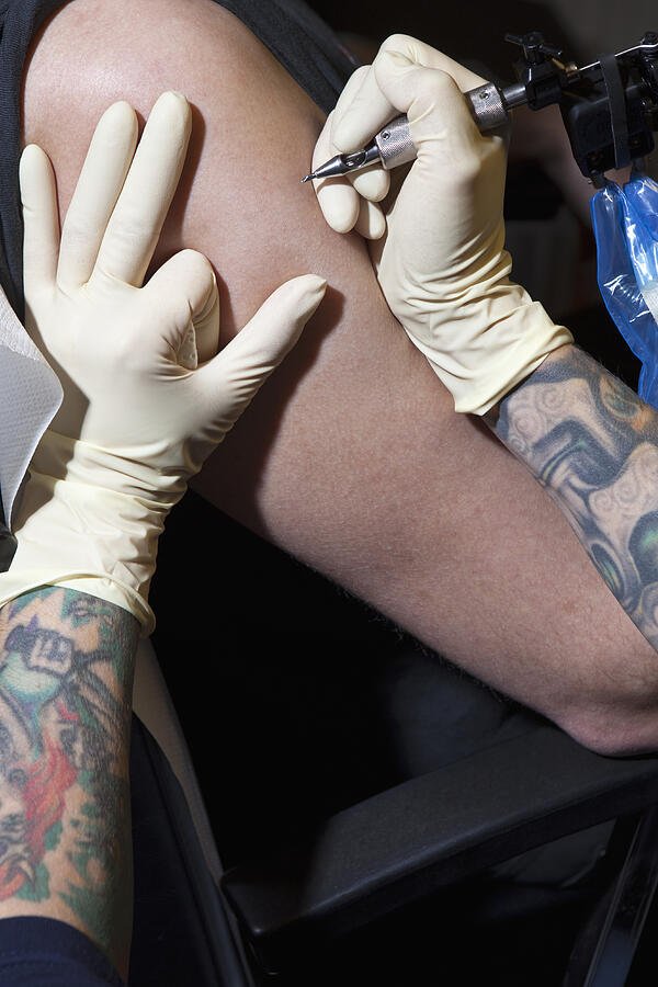 A tattoo artist preparing to tattoo a mans bare arm, close-up #1 Photograph by Halfdark