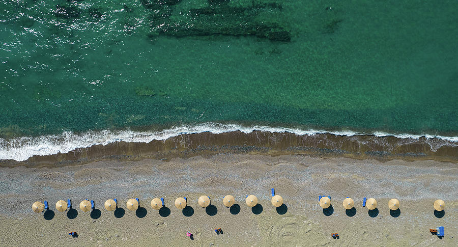 Aerial view from a flying drone of beach umbrellas in a row on an empty beach with braking waves. Photograph by Michalakis Ppalis