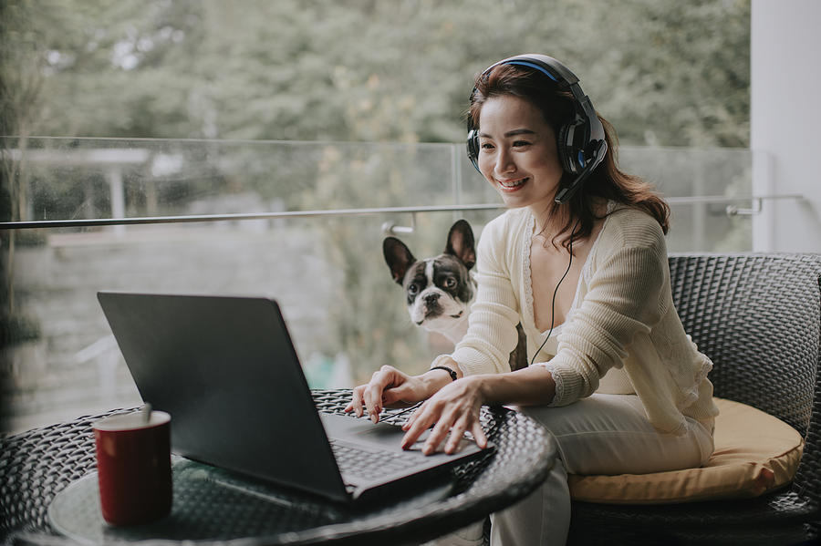 Asian Chinese Beautiful Woman Work From Home Having Virtual Meeting With Colleague At Balcony With Her Pet French Bulldog Wearing Headset #1 Photograph by Edwin Tan