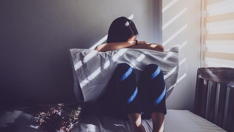 Asian women are sitting hugging their knees in bed. Feeling sad, disappointed in love In the dark bedroom and sunlight from the window through the blinds.Vintage tone. #1 Photograph by Bunditinay