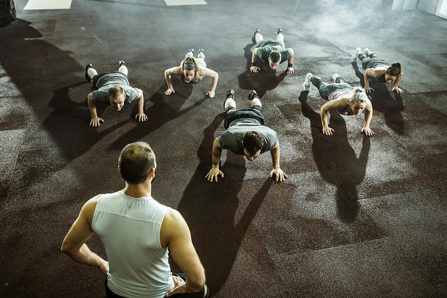 Athletic people doing push-ups on sports training with their coach. #1 Photograph by Skynesher