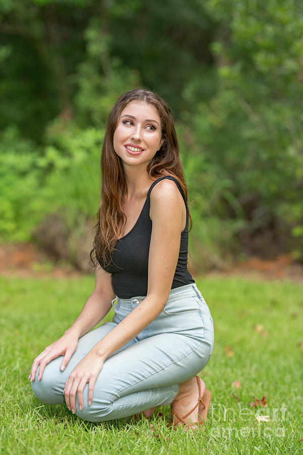 Attractive woman squatting in a park scene wearing tank top and ...