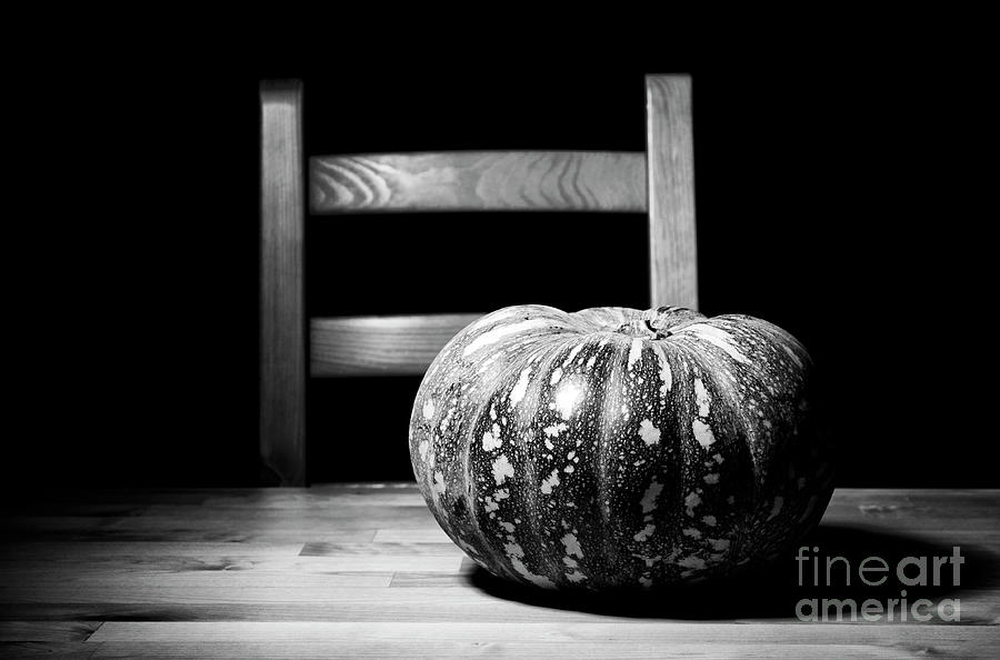 Black and white solitary pumpkin on rustic table with chair. #1 Photograph by Milleflore Images
