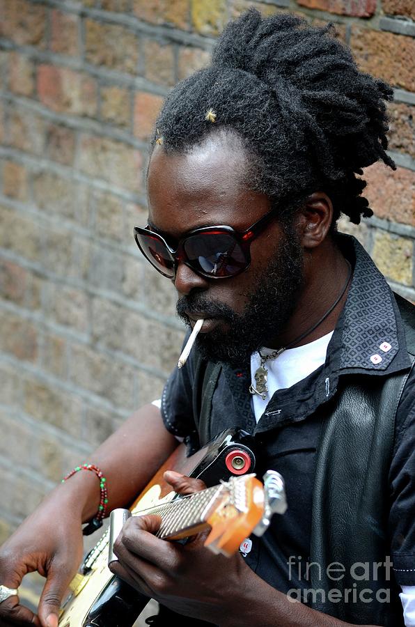 Black street musician sits against wall plays guitar London England #2 Photograph by Imran Ahmed