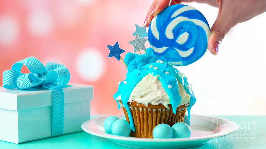 Blue novelty cupcake decorated with candy and large lollipops. #1 Photograph by Milleflore Images
